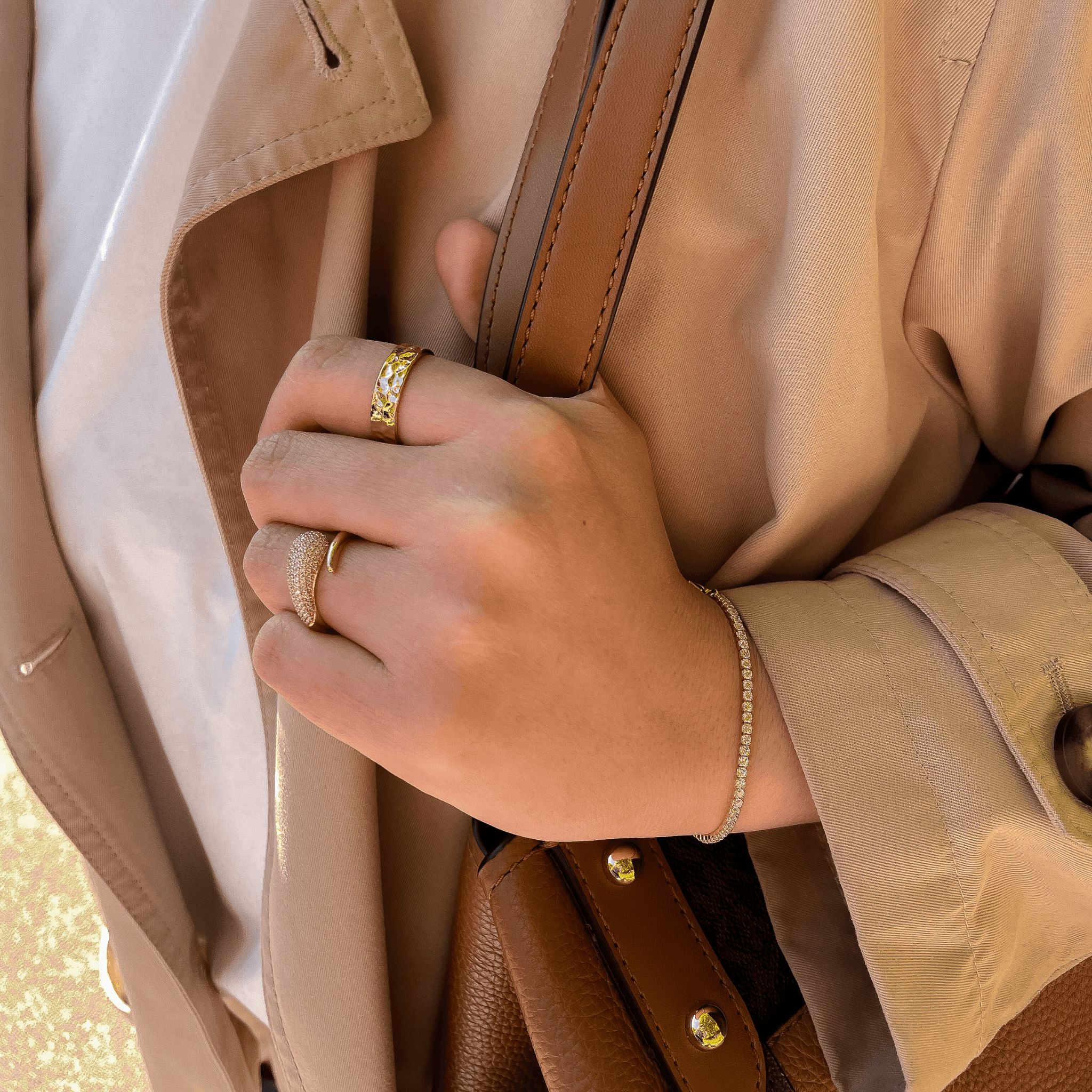 main féminine portant deux bagues en plaqué or et un bracelet tennis avec oxydes de zirconium blancs, tenue beige élégante