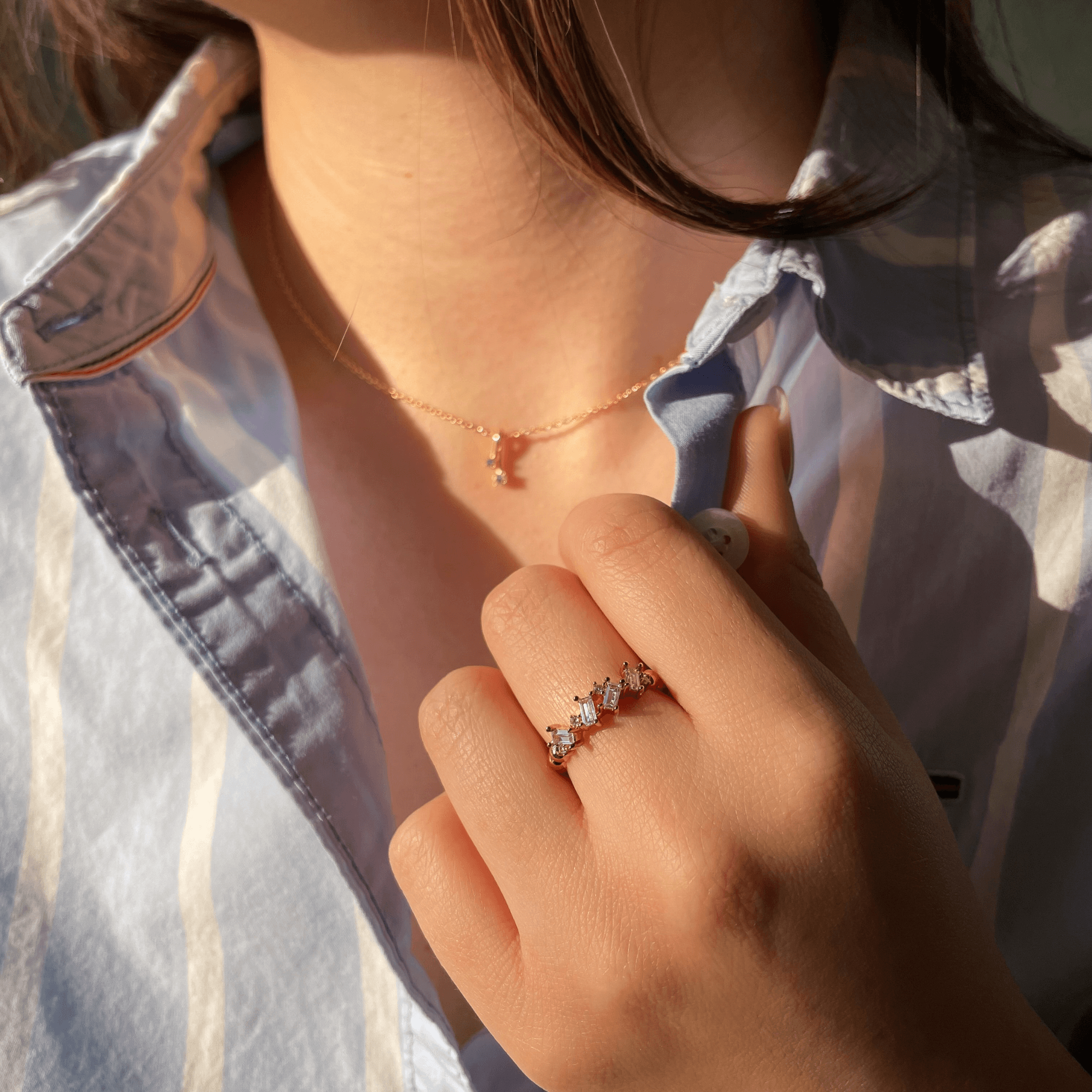 Bague en plaqué or sertie d’oxydes de zirconium blancs portée au doigt, avec lumière naturelle et chemise rayée