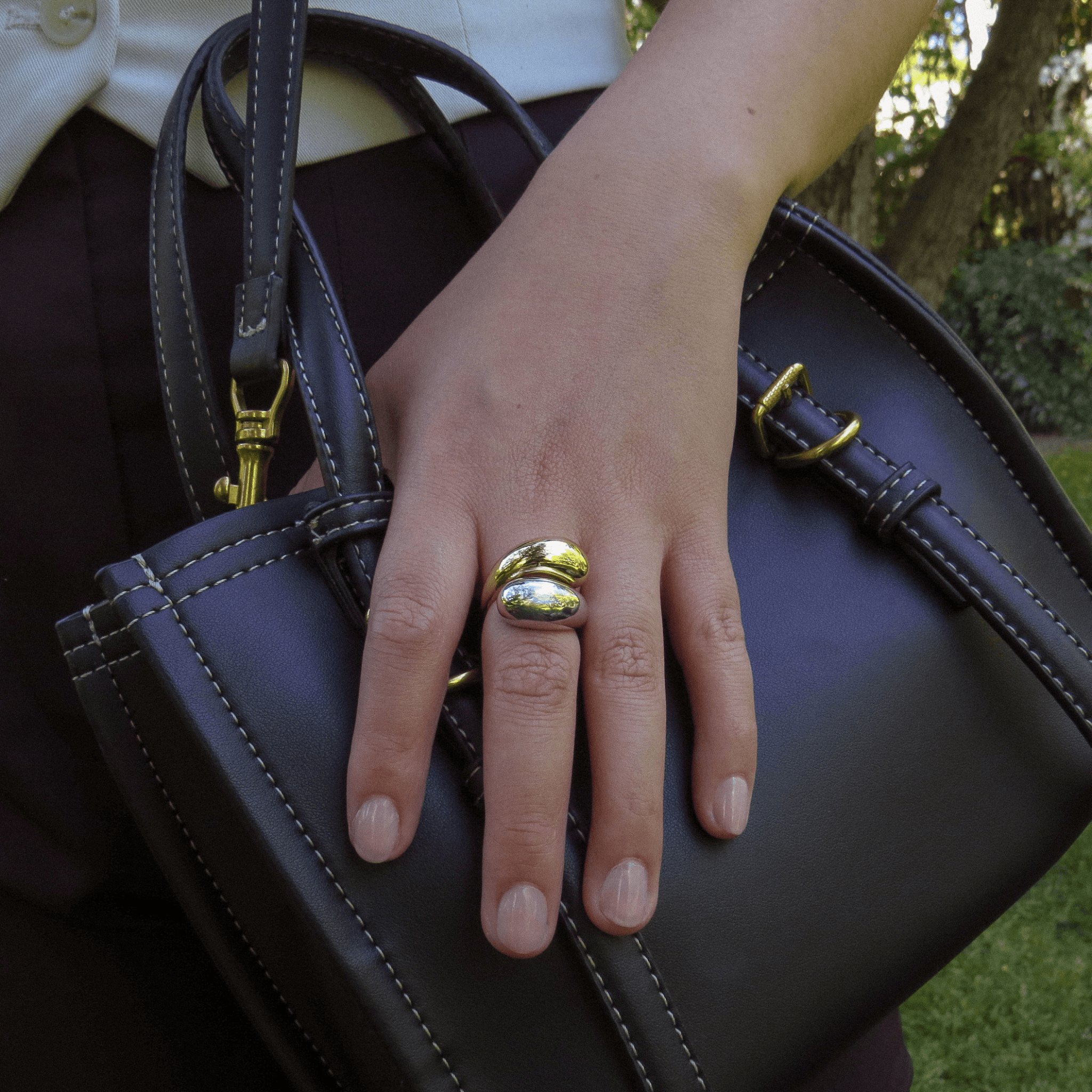 main avec bague en plaqué or et argent 925 au design bombé et lisse, portée sur un sac à main noir avec détails dorés