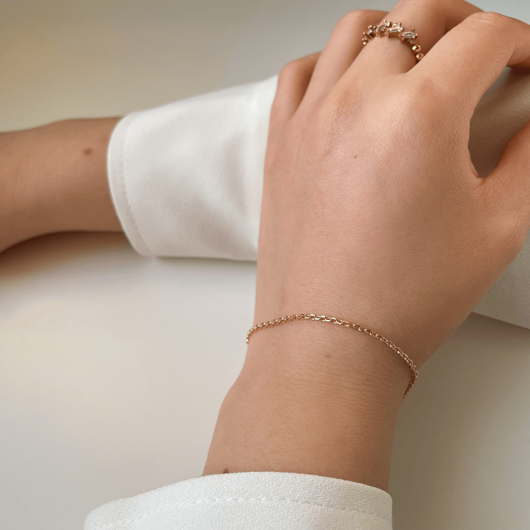 Bracelet fin en plaqué or porté au poignet, avec manche blanche et bague sertie d’oxydes de zirconium