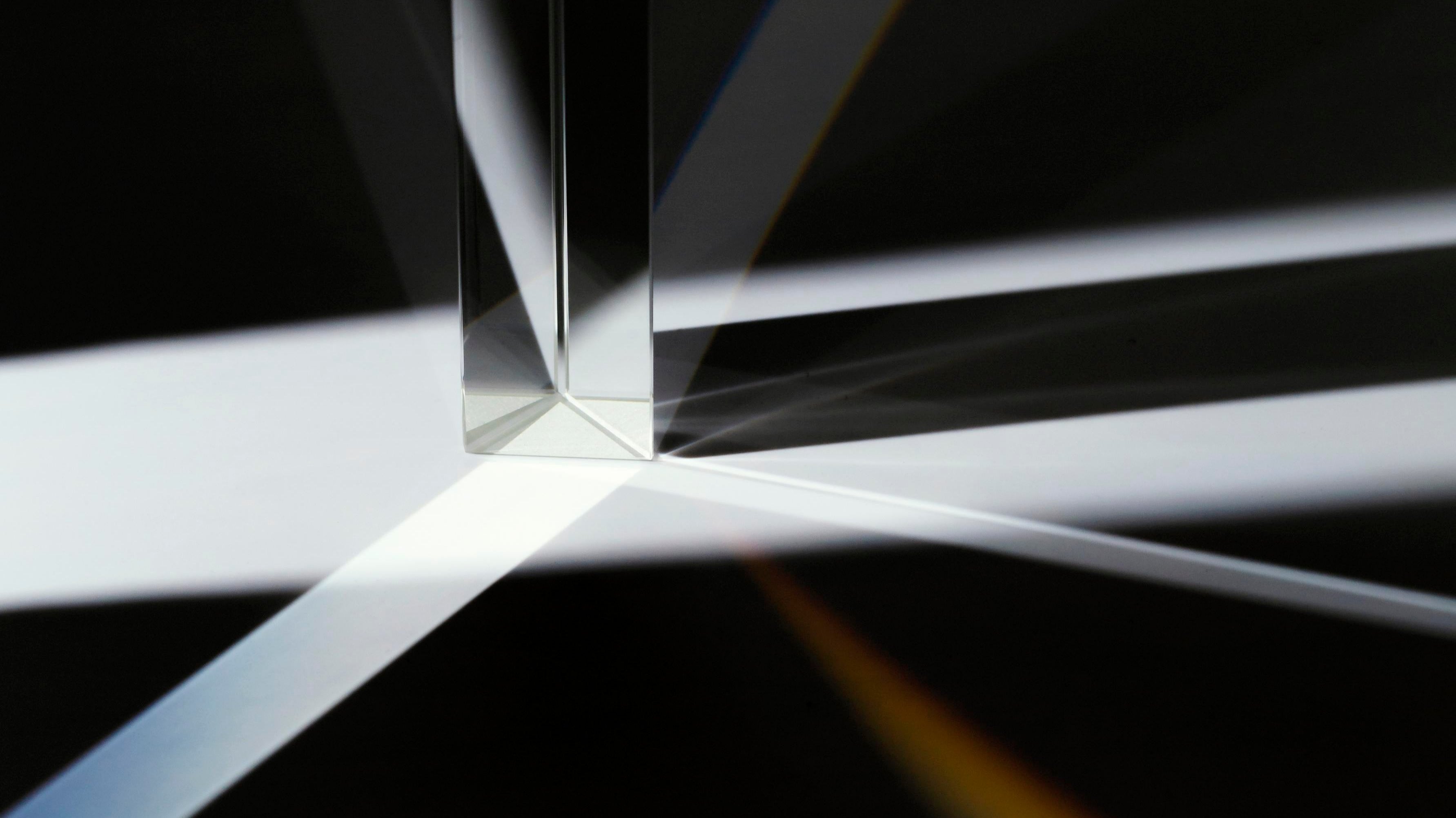 Prisme en verre projetant des rayons lumineux blancs sur fond sombre, symbole d’éclat et de clarté.