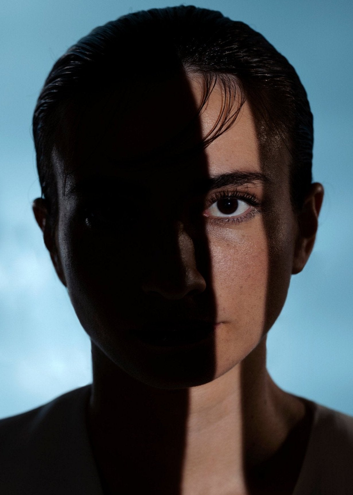 Portrait de femme à moitié dans l’ombre, traversée par une lumière verticale, symbolisant la dualité.