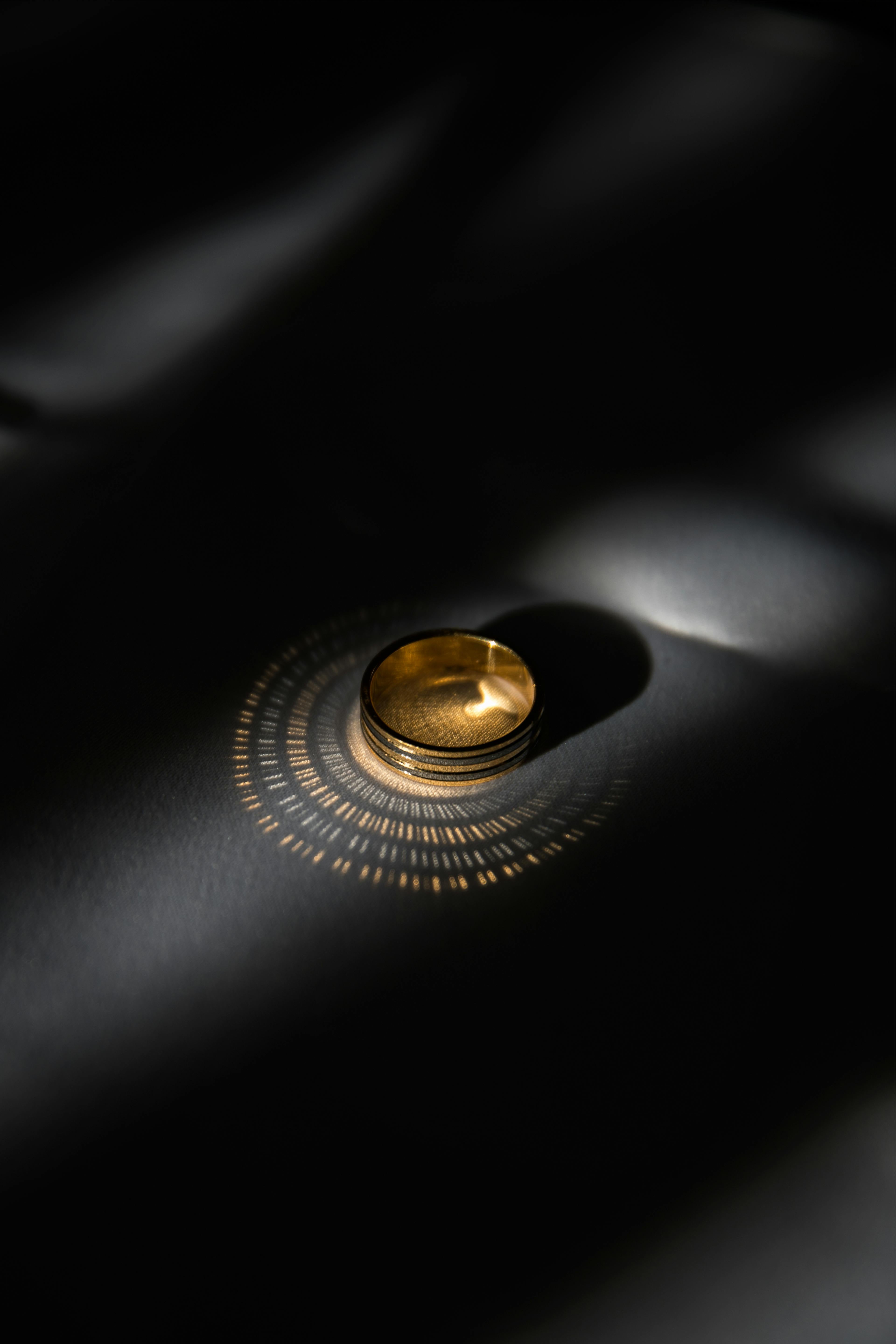 Bague dorée éclairée dans l’obscurité, projetant un motif circulaire lumineux – qualité et matière.